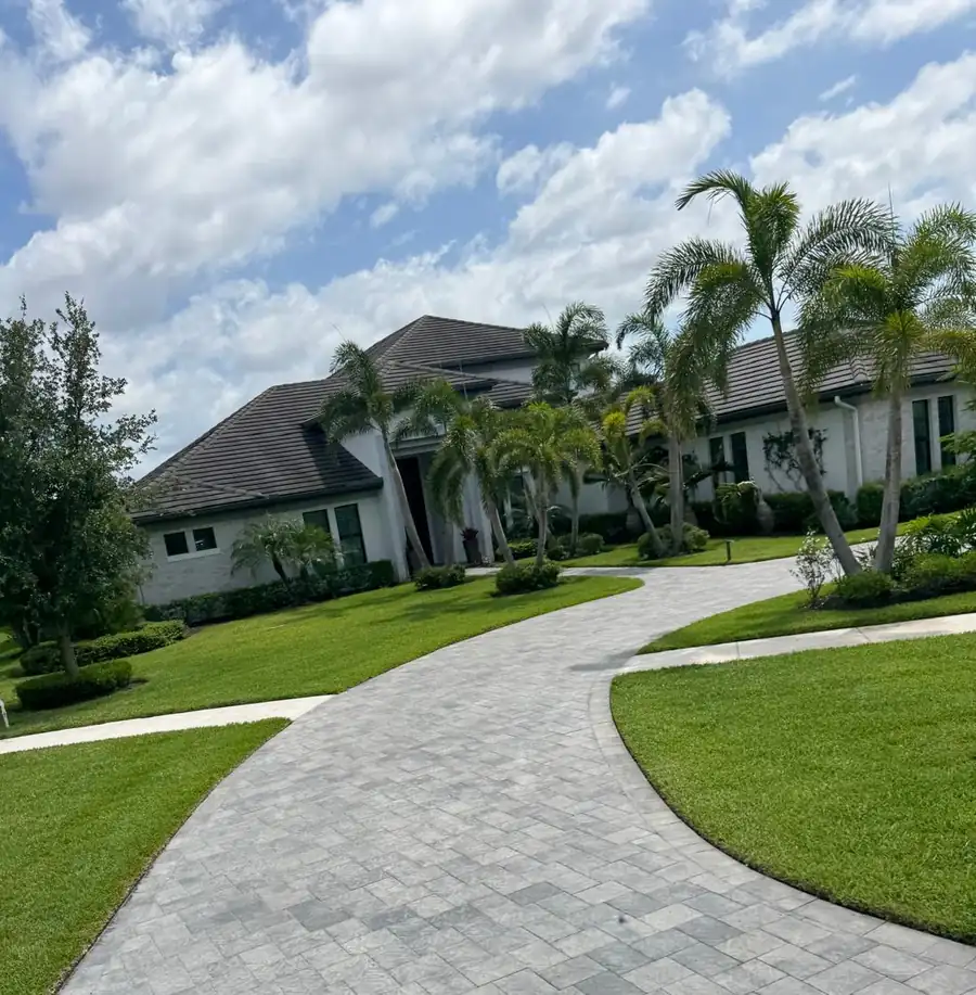 Palm-lined home with a curved paver driveway and a well-kept lawn
